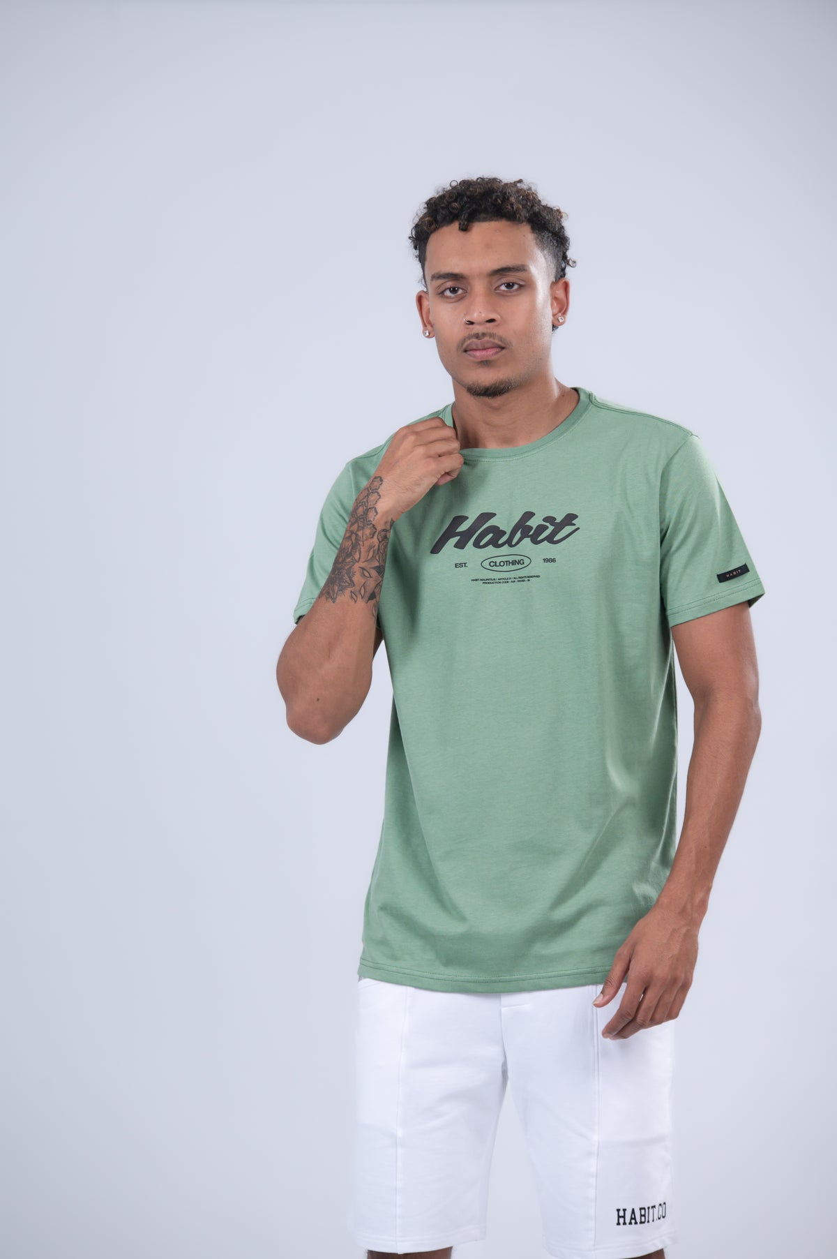 A sage green short-sleeve t-shirt with a black 'Habit' graphic on the chest.