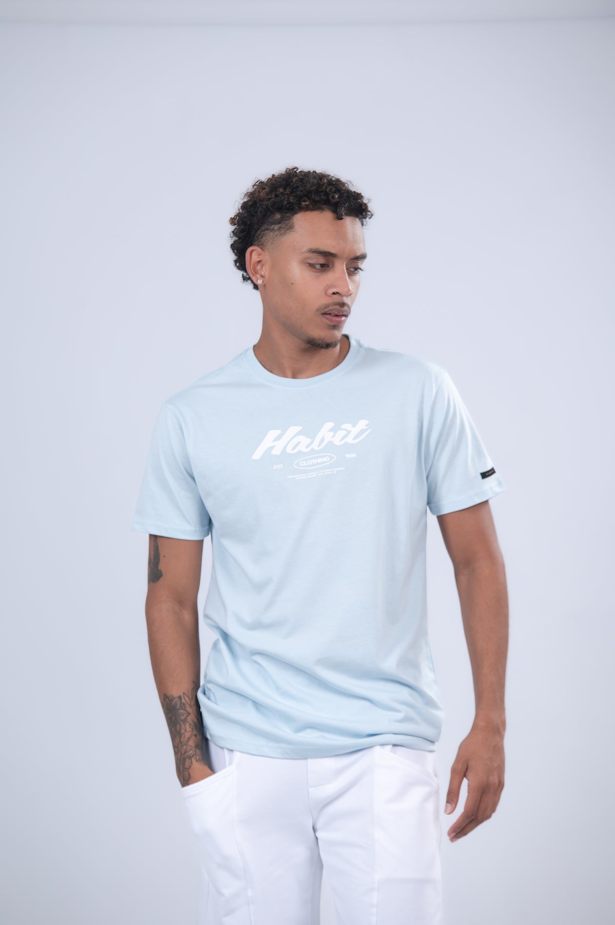 A light blue short-sleeve t-shirt with 'Habit' printed in white script across the chest.